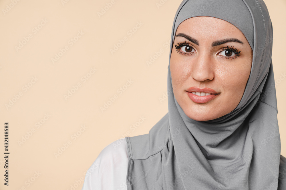 Close up cropped portrait of a beautiful young muslim Middle Eastern islamic arabian woman in grey hijab isolated over beige background. Islam confession religion Close up cropped portrait of a beautiful young muslim Middle Eastern islamic arabian woman in grey hijab isolated over beige background. Islam confession religion