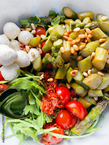 Fresh vegeratian salad with green asparagus, mozarella, tomatoes, arugula and pine nuts. Healthy lunch food or salad for barbecue. Top view. photo