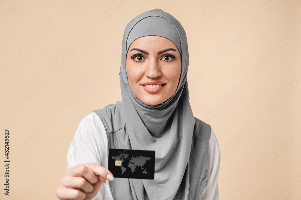 Smart middle eastern islamic arabian muslim young female in grey hijab bank  customer holding credit card for online shopping isolated over beige  background. Debit and credit, loan transactions Stock Photo | Adobe