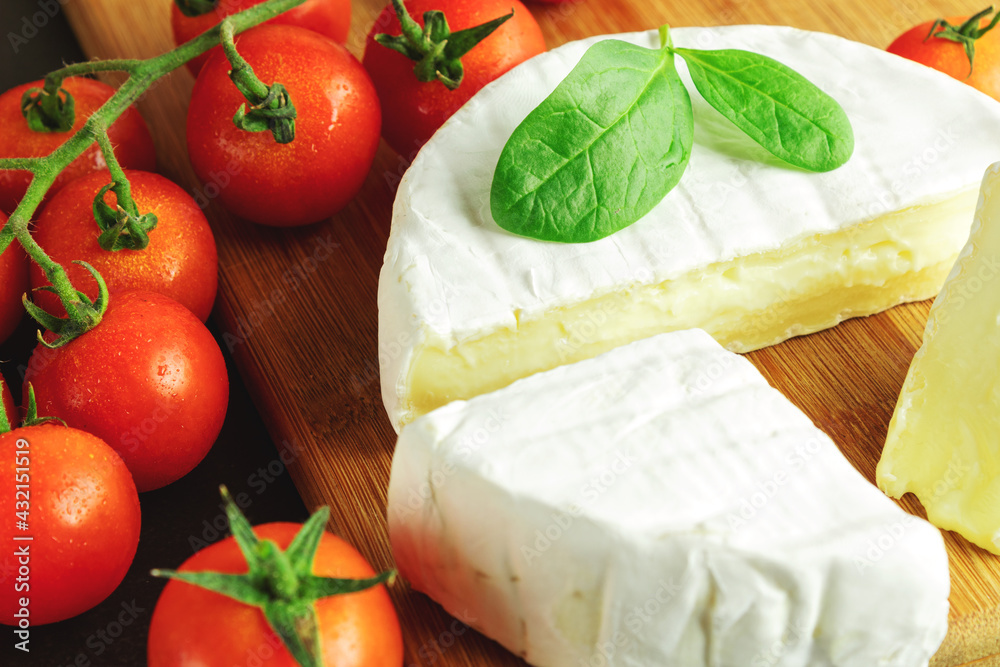 Camembert cheese with cherry tomatoes in a close-up, white blue cheese on a dark background, still life