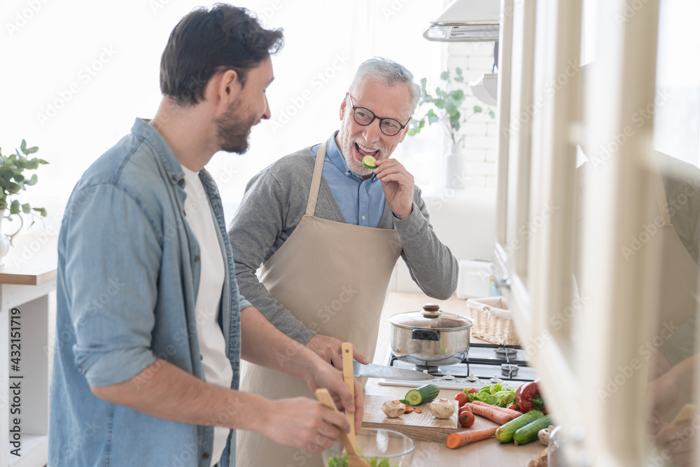 Happy young son helping his old elderly senior father in the kitchen to ...