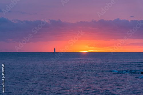 Glowing sunset over tropical ocean with silhouette of sailboat 