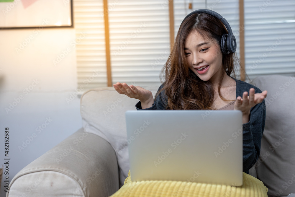 Cute young asian girl working on her lap top from the comfort of her home. She is in her sweater sitting on her couch. She is listening to music while smiling. Cute young asian girl working on her lap top from the comfort of her home. She is in her sweater sitting on her couch. She is listening to music while smiling.