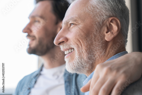 Close up shot of a caucasian young adult son supporting his old elderly senior man looking at the window in future together at home. Happy father`s day! I love you, dad!