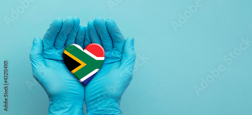 Doctors hands wearing surgical gloves holding South Africa flag heart