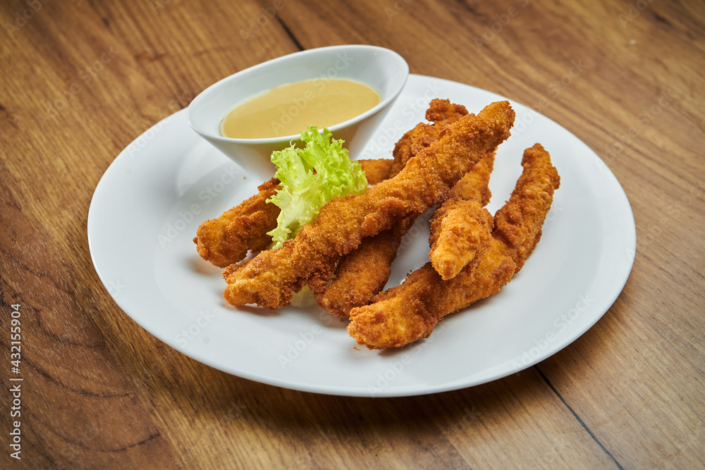 Deep-fried, breaded chicken nuggets, served in a white plate with honey mustard sauce in a white plate Deep-fried, breaded chicken nuggets, served in a white plate with honey mustard sauce in a white plate