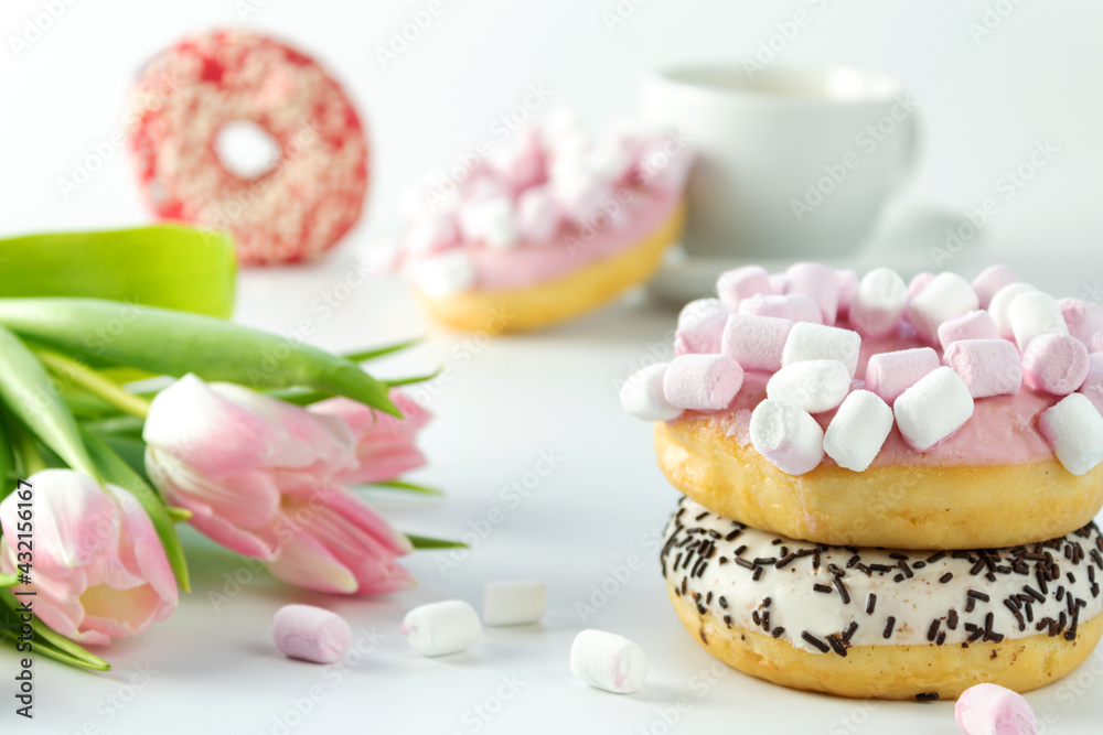 Sweet donuts with marshmallows and tulips flowers, on a white background, scattered marshmallows, close-up view from the front