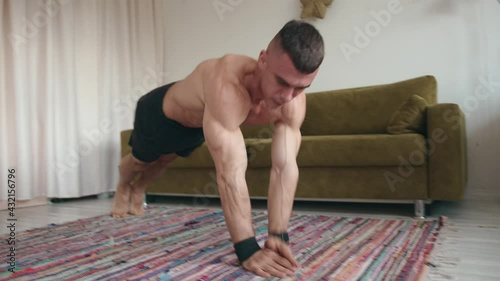 Young naked torso bodybuilder training at home and doing push-ups by moving his arms on the mat