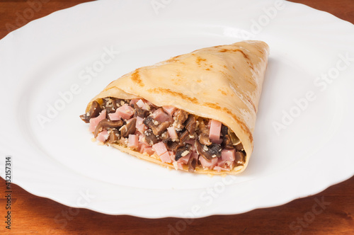 crepe with ham, mushrooms and cheese on a white plate