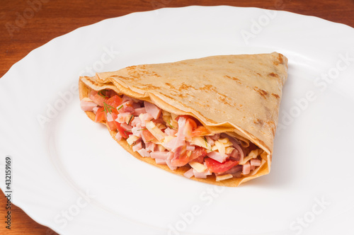 crepe with tomatoes ham and cheese on a white plate