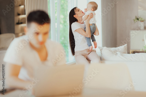 Young mother looks after her baby while her husband works on laptop
