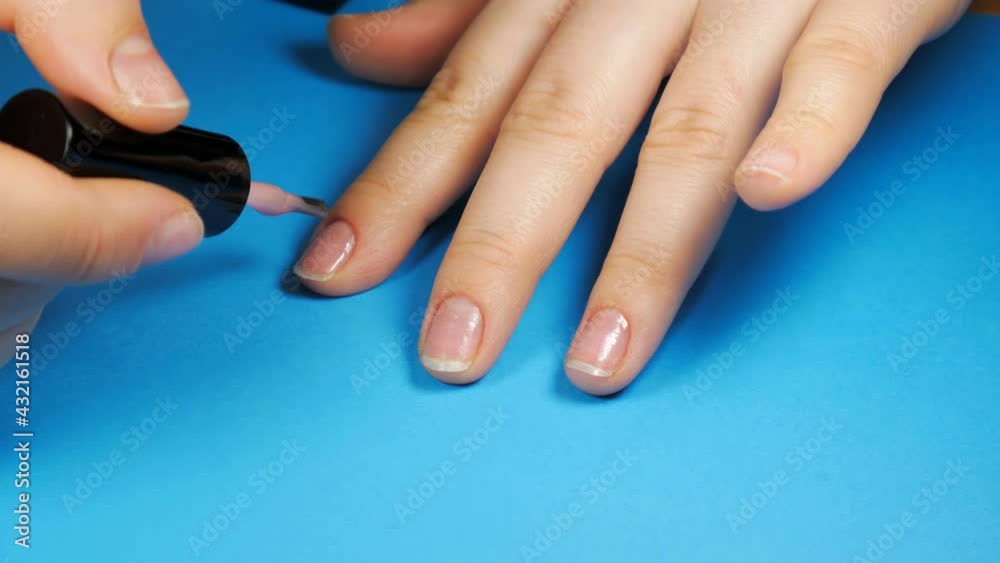 Young girl paints her nails with light pink nail polish On a blue background in home. Make yourself a manicure. Young girl paints her nails with light pink nail polish On a blue background in home. Make yourself a manicure.