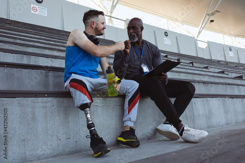 African american male coach and caucasian male athlete with prosthetic leg fist bumping in stadium photo