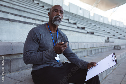 African american male coach with stopwatch measuring time while sitting on the seats in the stadium photo