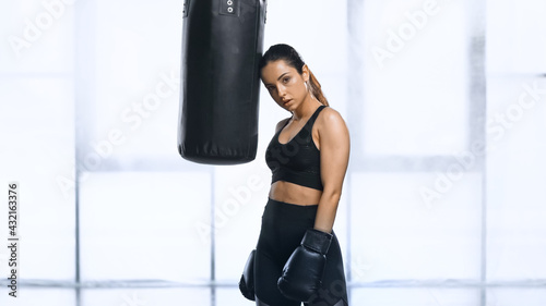 exhausted sportswoman in boxing gloves and sportswear leaning on punching bag. © LIGHTFIELD STUDIOS