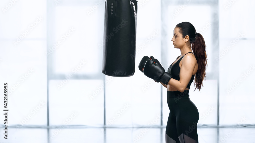 side view of sportswoman training with punching bag in gym.