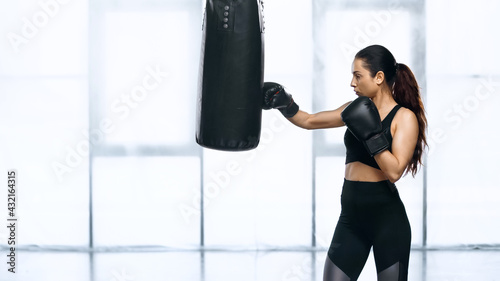 side view of young sportswoman training with punching bag in gym.