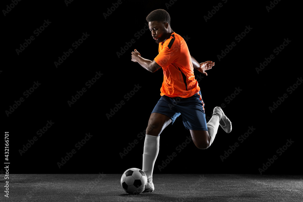 Young African football soccer player playing isolated on black background. Concept of sport, movement, energy and dynamic. Young African football soccer player playing isolated on black background. Concept of sport, movement, energy and dynamic.