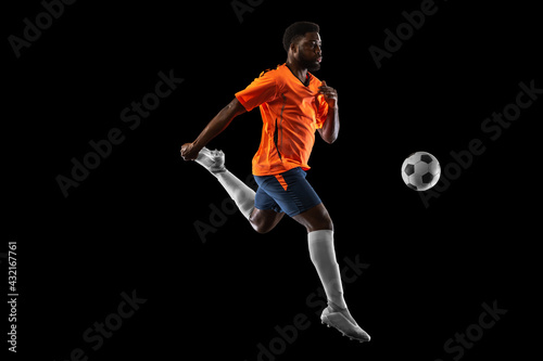 Young African football soccer player playing isolated on black background. Concept of sport, movement, energy and dynamic.