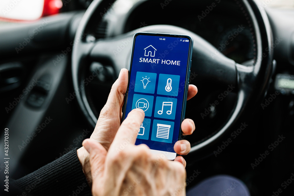 Woman driver using smart home app on smartphone in car - Internet of Things (IOT) concept