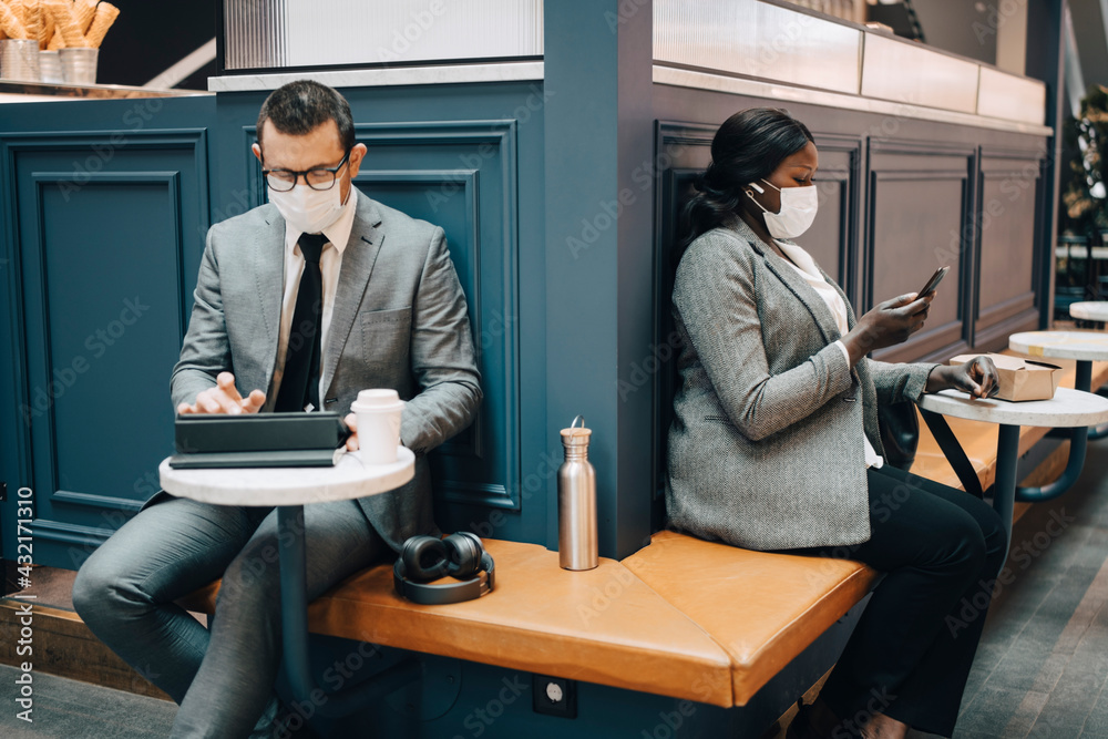 Businessman using digital tablet while female colleague with smart phone in cafe during COVID-19 Businessman using digital tablet while female colleague with smart phone in cafe during COVID-19