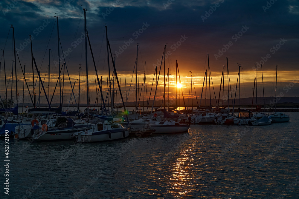 Sailboats in the harbor dock in the light of the setting sun; color illustration photo of tourism.