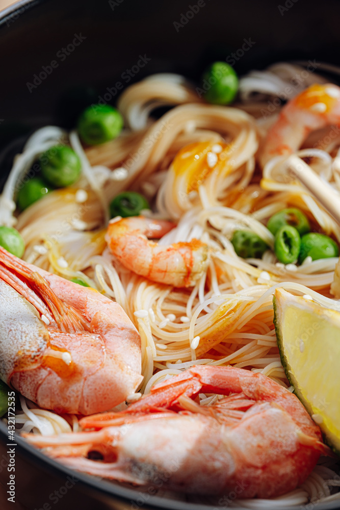 romantic dinner for two. Asian cuisine, rice noodles with shrimp and seafood, green peas and onions. soy sauce and various fresh vegetables. romantic dinner in black plates with Japanese chopsticks romantic dinner for two. Asian cuisine, rice noodles with shrimp and seafood, green peas and onions. soy sauce and various fresh vegetables. romantic dinner in black plates with Japanese chopsticks