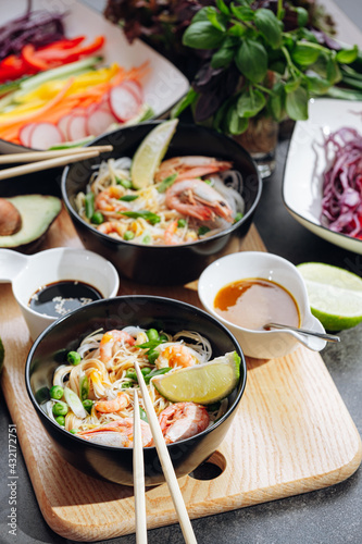 romantic dinner for two. Asian cuisine, rice noodles with shrimp and seafood, green peas and onions. soy sauce and various fresh vegetables. romantic dinner in black plates with Japanese chopsticks