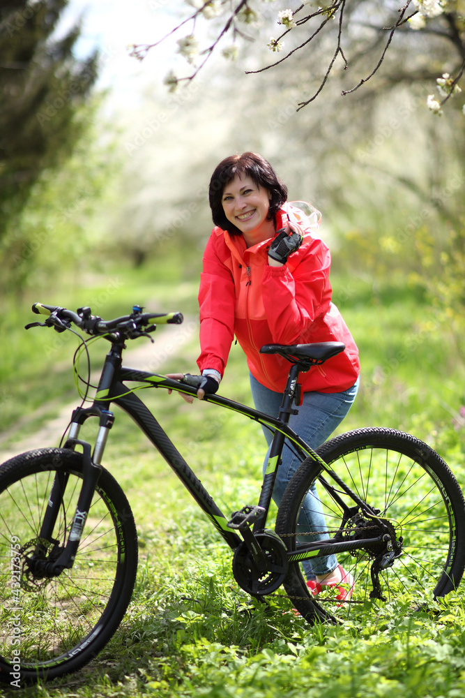 Fototapeta premium Beautiful woman on a bike in a blooming spring garden. Beautiful mature woman posing for the camera in a blooming spring garden.