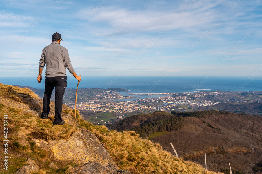 A young man in a gray sweater looking at the views of the towns of Hondarribia and Hendaya from the mountains of Aiako Harria or Peñas de Aya, Guipúzcoa. Basque Country