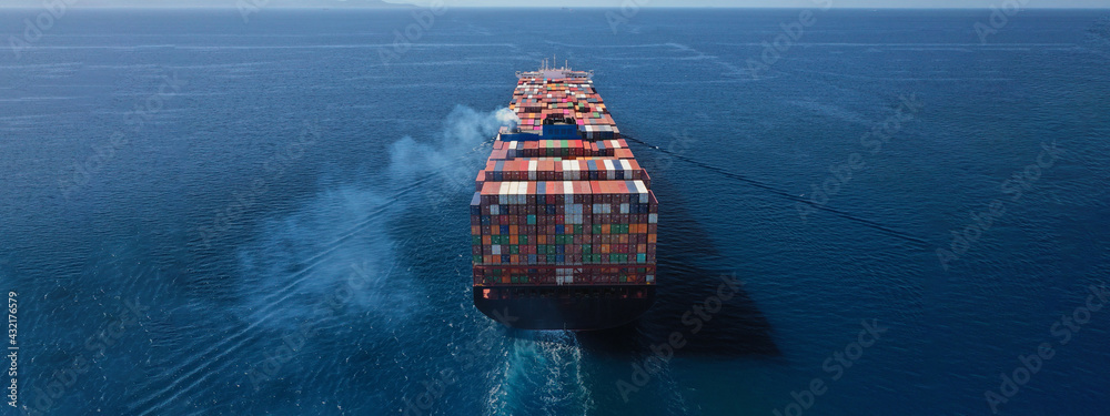 Aerial drone ultra wide photo above huge colourful container carrier vessel cruising deep blue open ocean sea