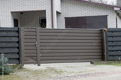 one brown large metal gate and part of a black wooden fence outside