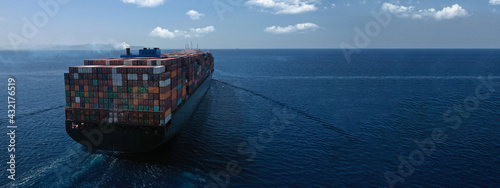 Aerial drone ultra wide photo above huge colourful container carrier vessel cruising deep blue open ocean sea