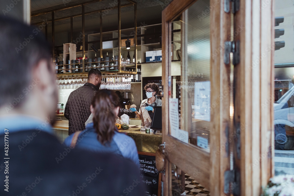 Customers maintaining social distancing while collecting order from deli store during pandemic Customers maintaining social distancing while collecting order from deli store during pandemic