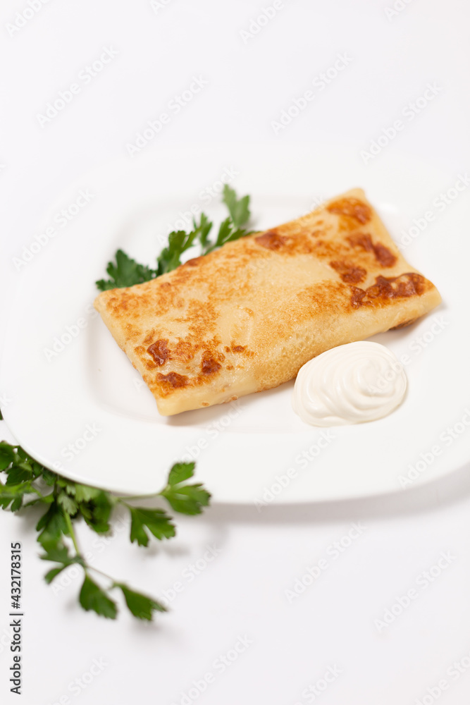 Fried pancake stuffed with sour cream and parsley on a white plate