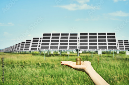 Hand holding money banknote with photovoltaic solar energy panels in background, 