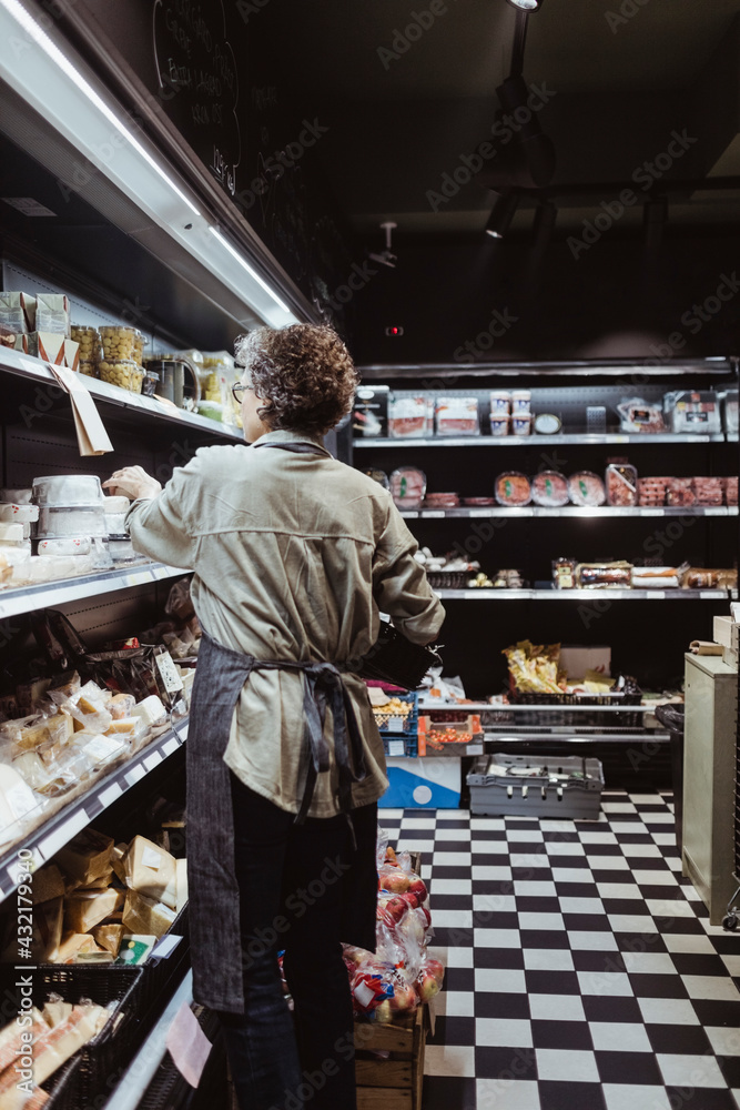 Rear view of female owner arranging product on rack at delicatessen shop Rear view of female owner arranging product on rack at delicatessen shop