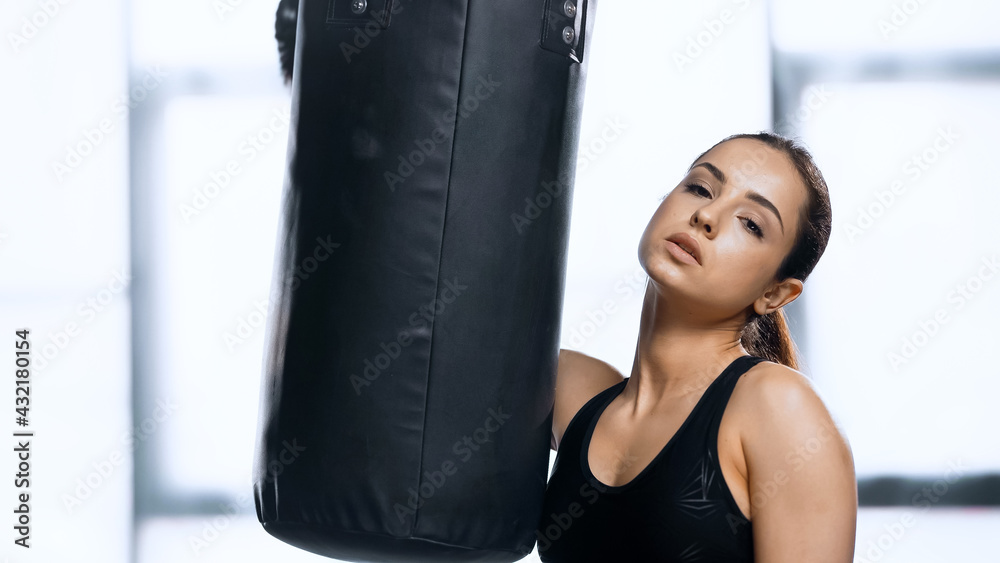 tired young woman in boxing glove resting near punching bag in gym.