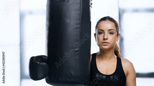 young sportswoman in boxing glove resting near punching bag in gym.