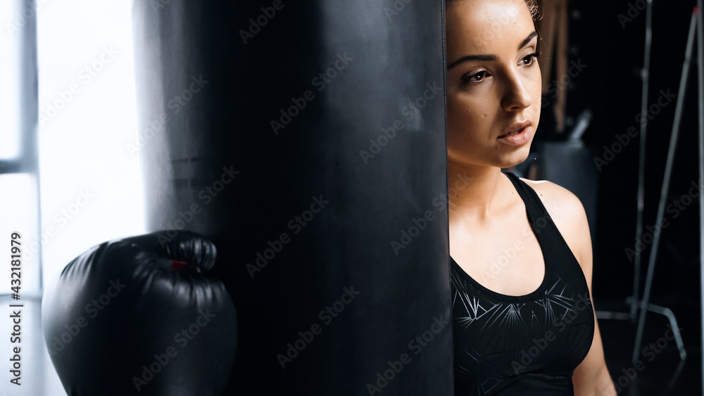 tired sportswoman in boxing glove leaning on punching bag.
