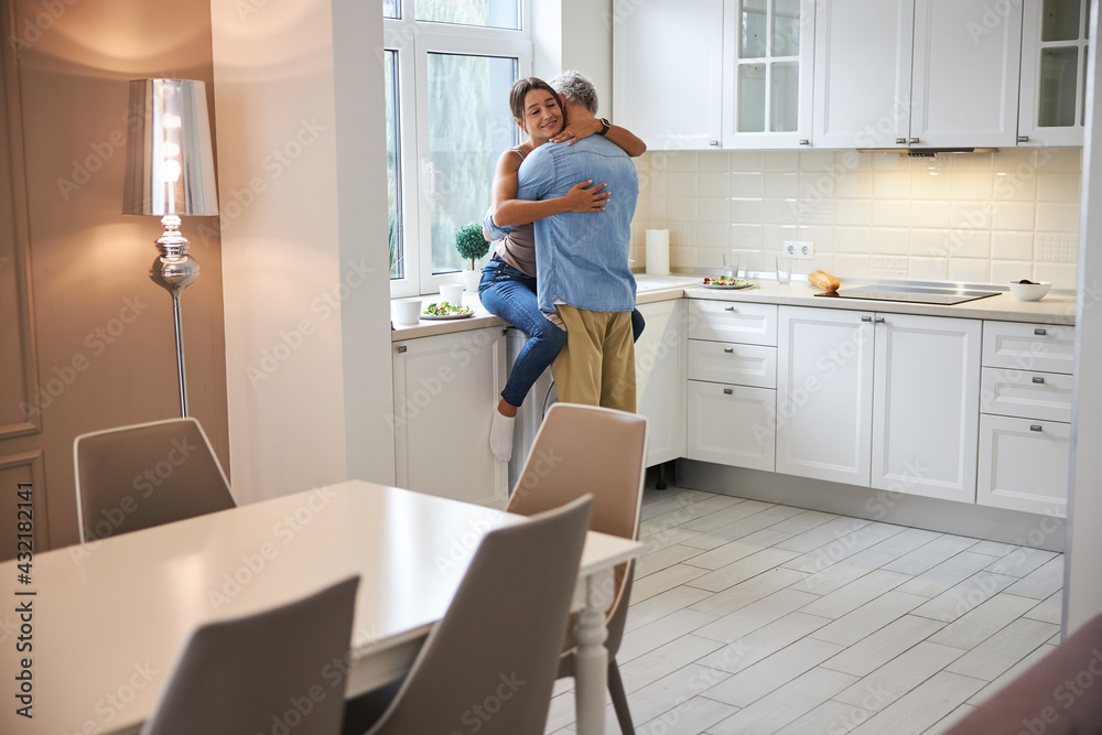 Pleased woman sitting on the table in kitchen Pleased woman sitting on the table in kitchen