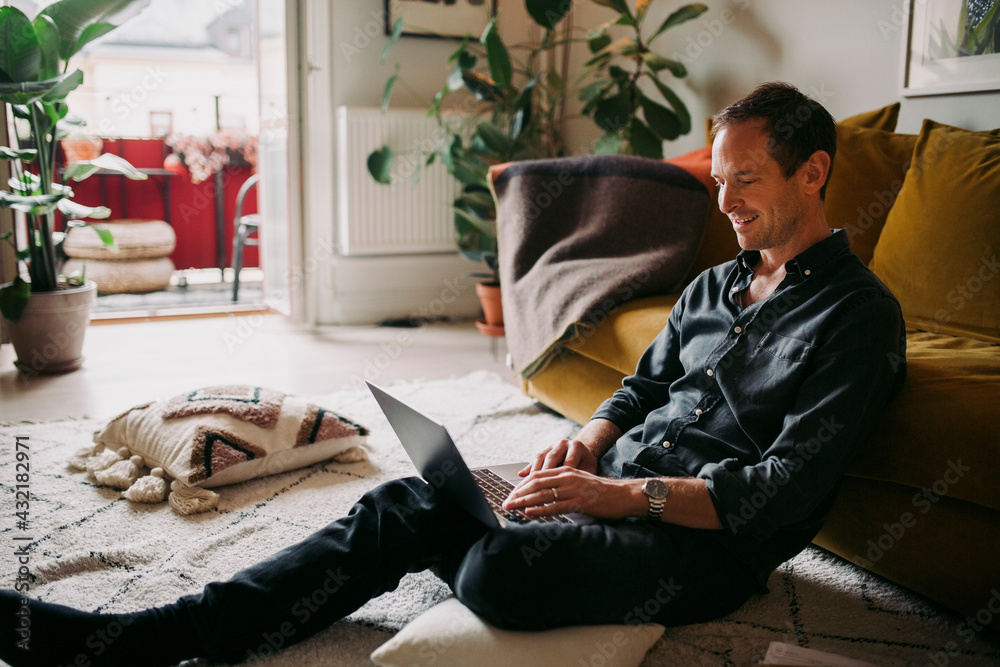 Smiling businessman working on laptop in living room Smiling businessman working on laptop in living room