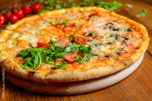 Italian pizza with cheese tomatoes, arugula and mushrooms on wooden cutting board stock photo.