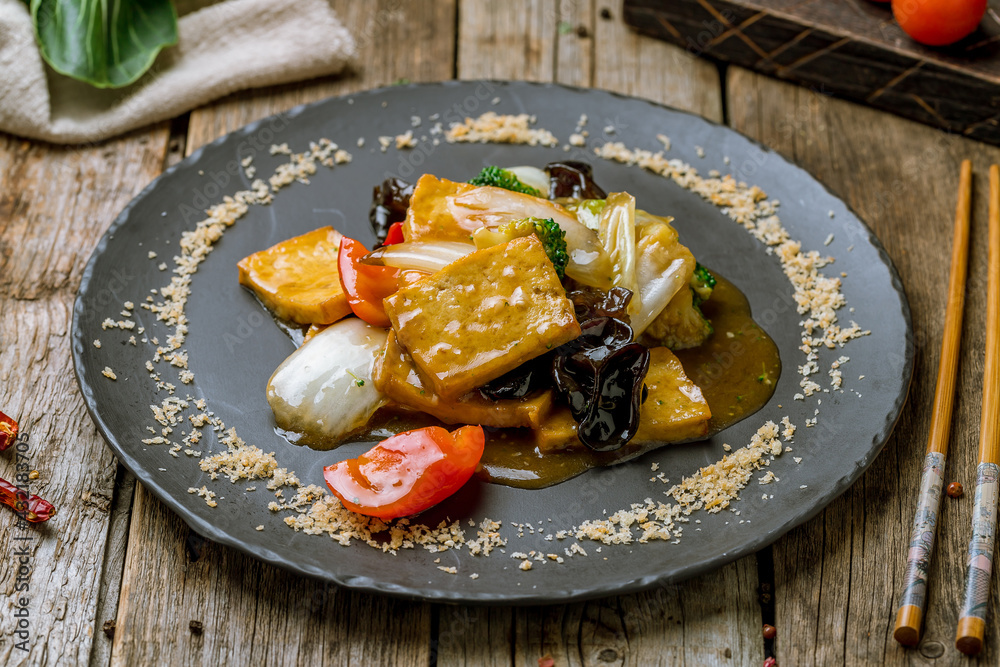 fried tofu with vegetables on black stone plate on old wooden table
