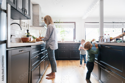 Mother doing chores while children standing in kitchen at home photo