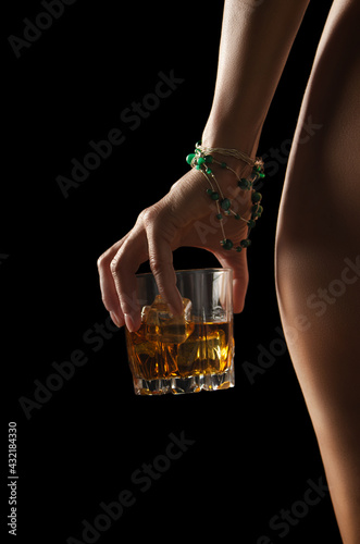 Obraz na płótnie Caucasian model holds glass of whiskey with icecubes in her hand near naked hip on dark background closeup studio shot w salonie
