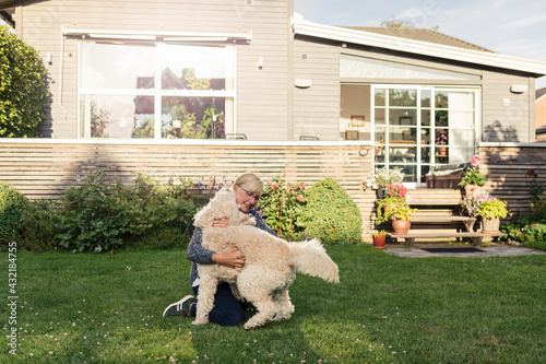 Mature woman embracing dog at front yard photo