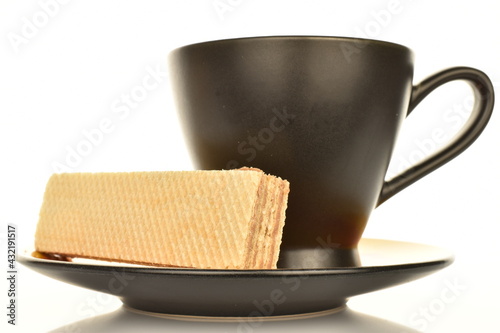 One sweet vanilla waffle with a black cup and saucer, close-up, isolated on white.