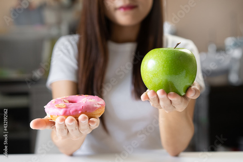 Woman on dieting for good health concept. Close up female comparing favourite donut and green apple for good health.