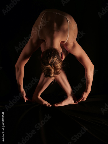 Naked woman in yoga pose on black isolated background with artificial professional lighting without face